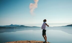 man standing on sand while spreading arms beside calm body of water