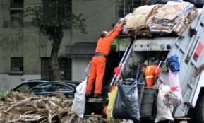 man in orange jacket and blue denim jeans standing near garbage