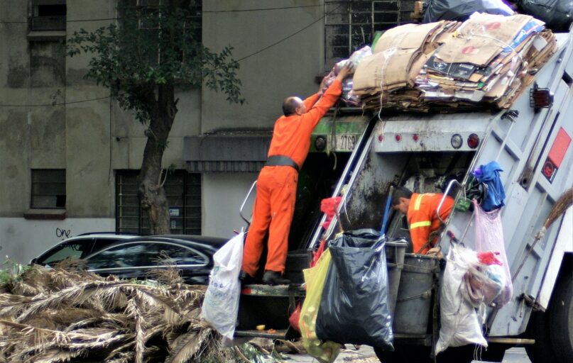 man in orange jacket and blue denim jeans standing near garbage