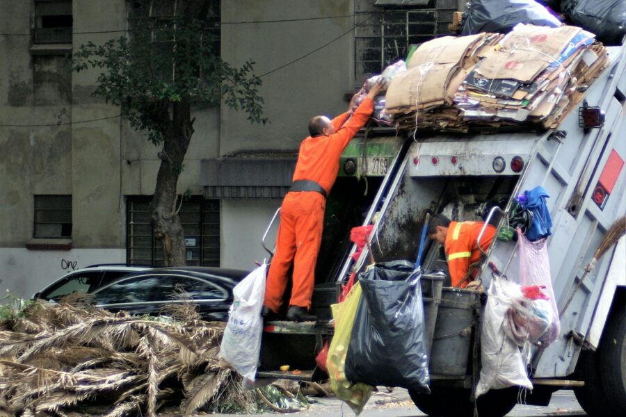 man in orange jacket and blue denim jeans standing near garbage