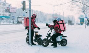 Delivery workers on scooters in snowy city street