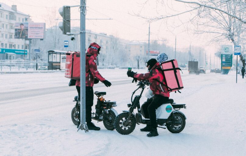 Delivery workers on scooters in snowy city street
