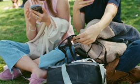 Two people sit using their phones and bags.