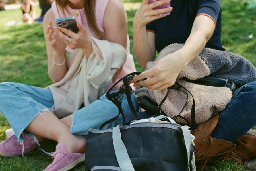 Two people sit using their phones and bags.