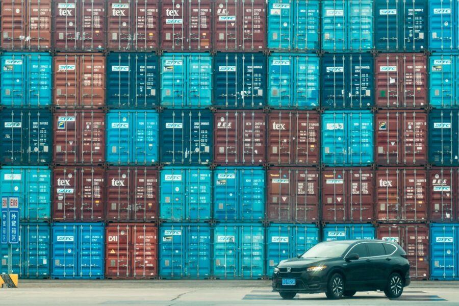 A car is parked in front of a large stack of shipping containers