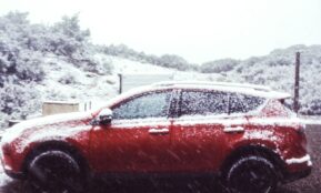 a red car parked on the side of a road covered in snow