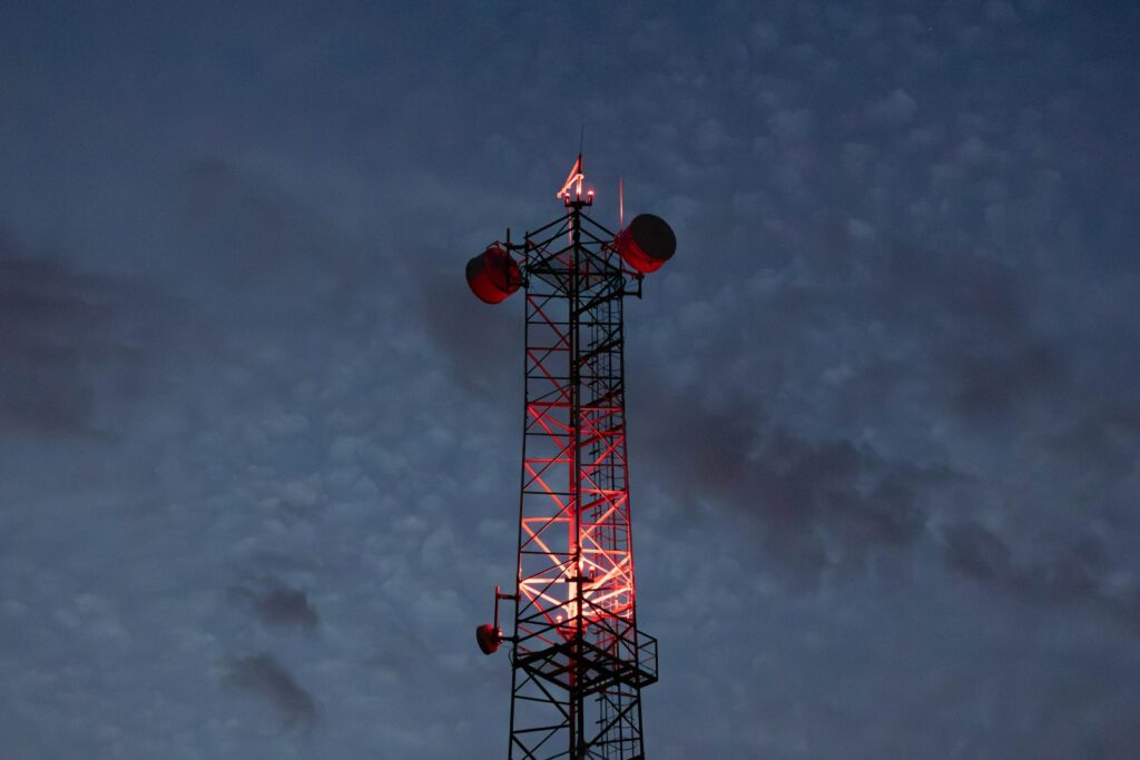 Cell tower illuminated with red lights against twilight sky