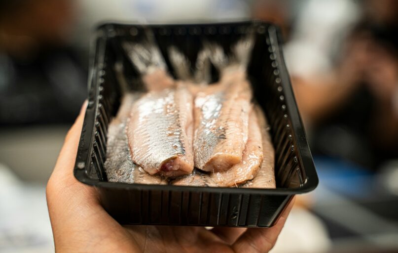 person holding black plastic tray with meat