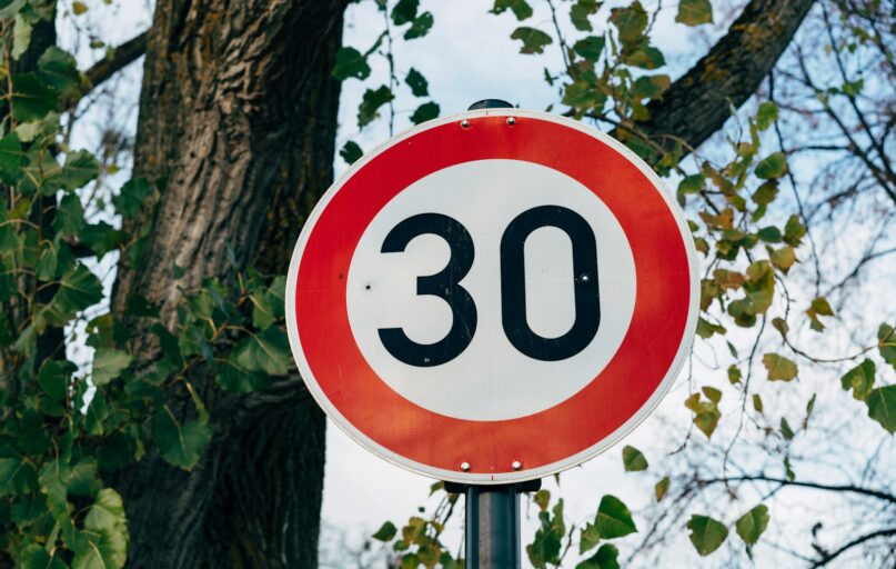 a red and white speed limit sign next to a tree
