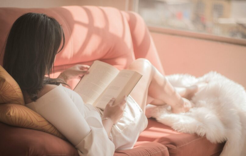 woman holding book sitting on pink fabric sofa
