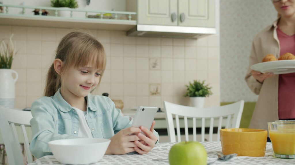 Girl using phone at kitchen table with breakfast