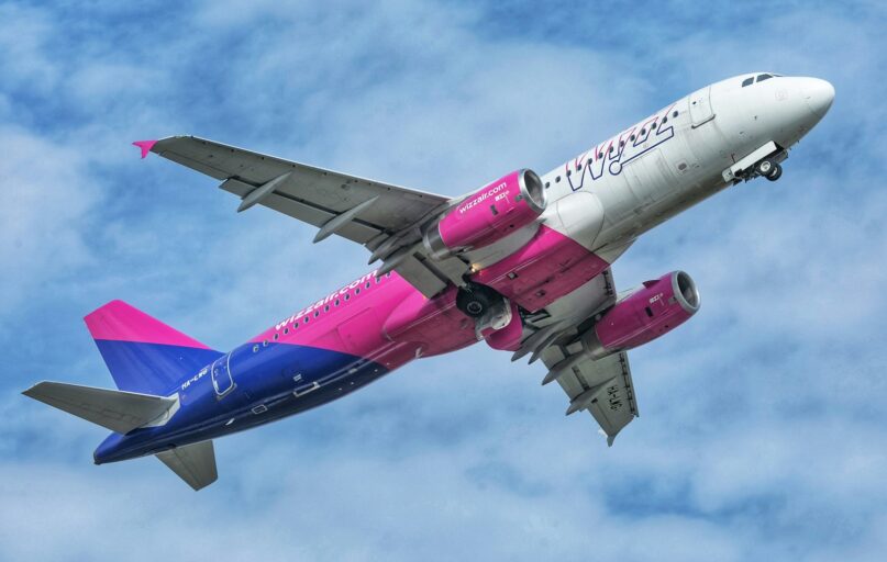 a pink and blue jet airliner flying in the sky