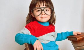 girl in red framed eyeglasses and gray sweater sitting on brown wooden chair