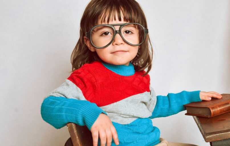 girl in red framed eyeglasses and gray sweater sitting on brown wooden chair