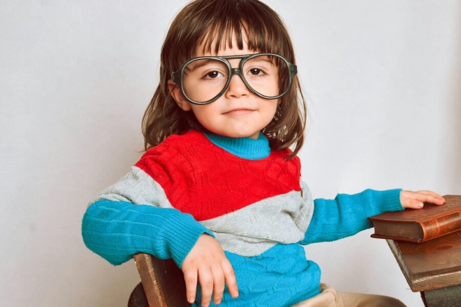 girl in red framed eyeglasses and gray sweater sitting on brown wooden chair
