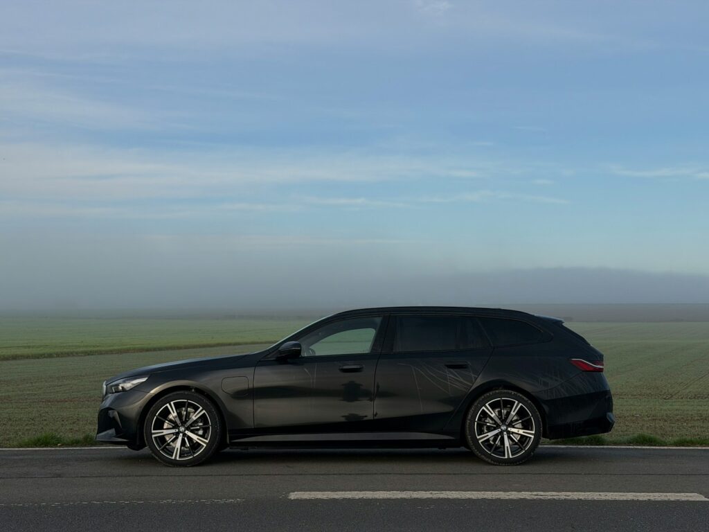 Dark station wagon parked on a road with misty fields.
