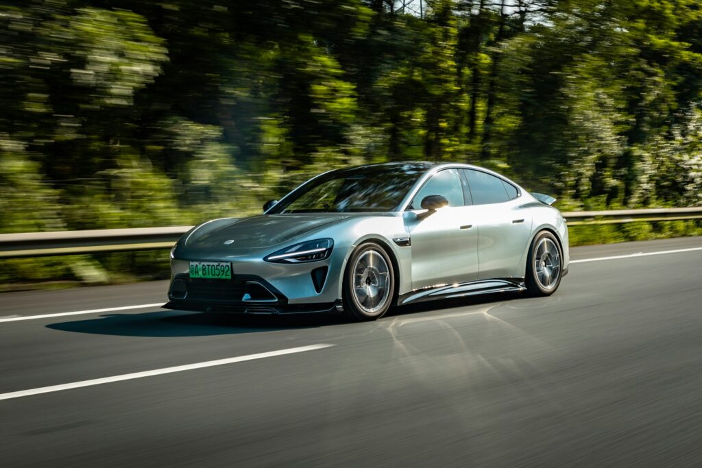A silver car driving down a road next to a forest