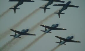 Six airplanes fly in formation, leaving smoke trails.