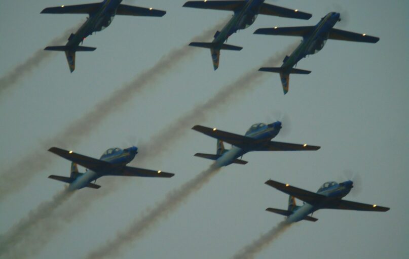 Six airplanes fly in formation, leaving smoke trails.