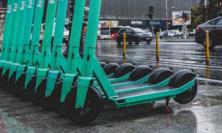 Rain-soaked electric scooters lined up on a city street, reflecting urban transportation.