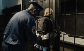 A police officer secures a prisoner in a dimly lit jail cell, emphasizing security.