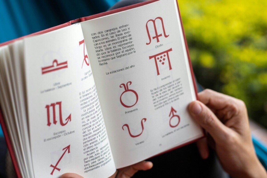 Open book displaying zodiac symbols and seasonal descriptions being held by hands.