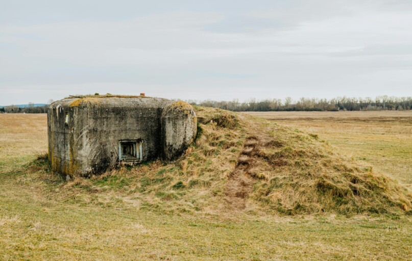 Concrete bunker covered with grass on a rural field, showcasing an abandoned, historical military structure.
