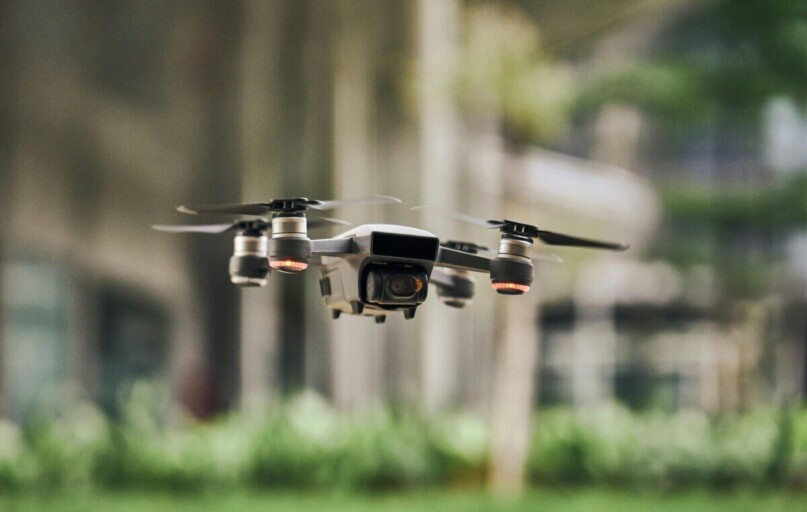 Close-up of a modern quadcopter drone hovering outdoors with blurred greenery background.