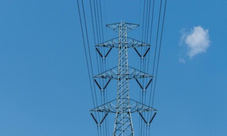 Low angle view of electric transmission tower and power lines under blue sky.