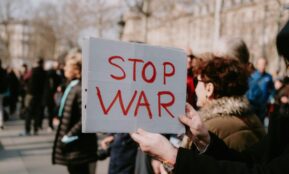 Crowd of people in a peaceful protest holding a 'Stop War' sign outdoors.
