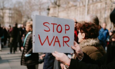 Crowd of people in a peaceful protest holding a 'Stop War' sign outdoors.