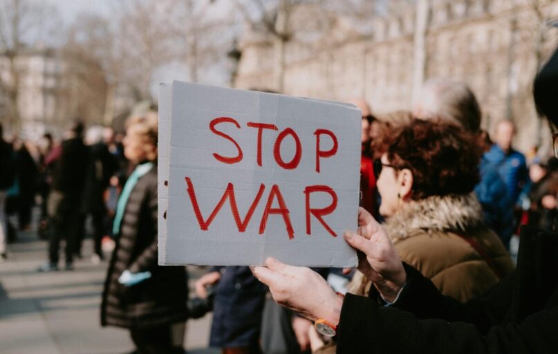 Crowd of people in a peaceful protest holding a 'Stop War' sign outdoors.