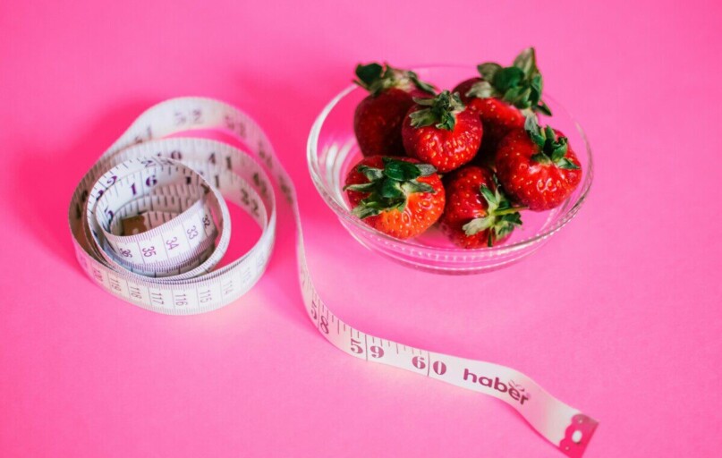 A glass bowl of fresh strawberries paired with a pink measuring tape symbolizes healthy eating.