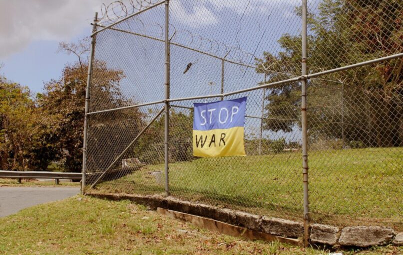 A protest banner with a "stop war" message hangs on a metal fence outdoors.