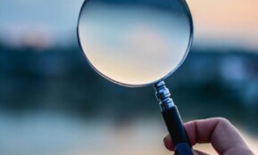 A magnifying glass held by a hand outdoors at sunset, focusing on exploration.