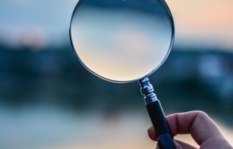 A magnifying glass held by a hand outdoors at sunset, focusing on exploration.