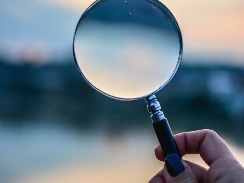 A magnifying glass held by a hand outdoors at sunset, focusing on exploration.