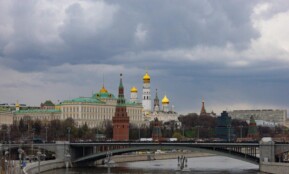 Dramatic view of the Kremlin and Moscow River bridge under cloudy skies, showcasing iconic architecture.