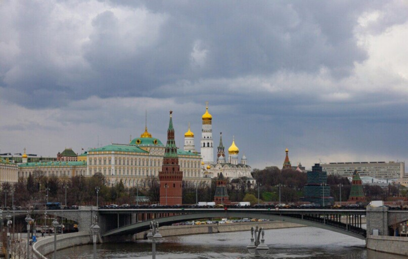 Dramatic view of the Kremlin and Moscow River bridge under cloudy skies, showcasing iconic architecture.