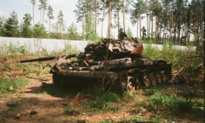 A destroyed military tank lies abandoned in a forest near Bucha, Ukraine amidst war-torn surroundings.