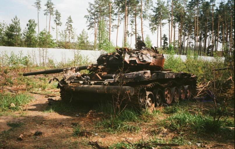 A destroyed military tank lies abandoned in a forest near Bucha, Ukraine amidst war-torn surroundings.