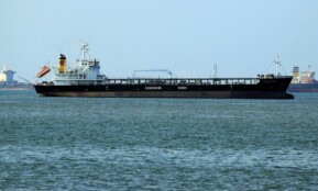 Oil tanker navigating calm ocean waters near a coastal harbor. Clear day view.