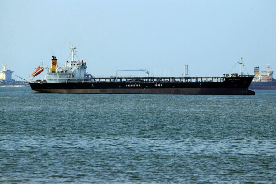 Oil tanker navigating calm ocean waters near a coastal harbor. Clear day view.