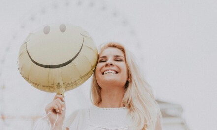 Cheerful woman holding a smiley balloon outdoors on a sunny day, exuding happiness and positivity.