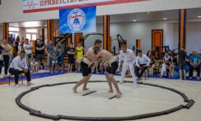 Young athletes engaged in sumo wrestling in a gym with spectators and a referee observing.