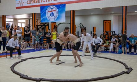 Young athletes engaged in sumo wrestling in a gym with spectators and a referee observing.