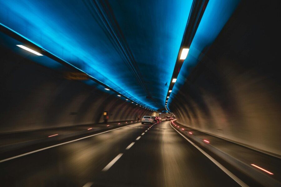 Long exposure capture of cars driving through a modern tunnel with blue lighting, showcasing speed and motion.
