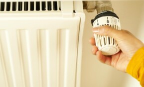 Close-up of hand adjusting radiator thermostat to control home heating temperature.