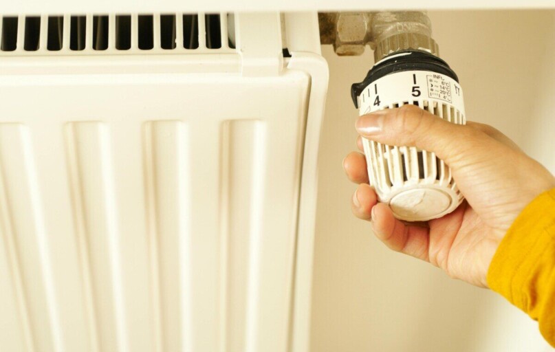 Close-up of hand adjusting radiator thermostat to control home heating temperature.
