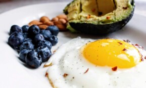 A nutritious breakfast featuring a fried egg, avocado, blueberries, and almonds.